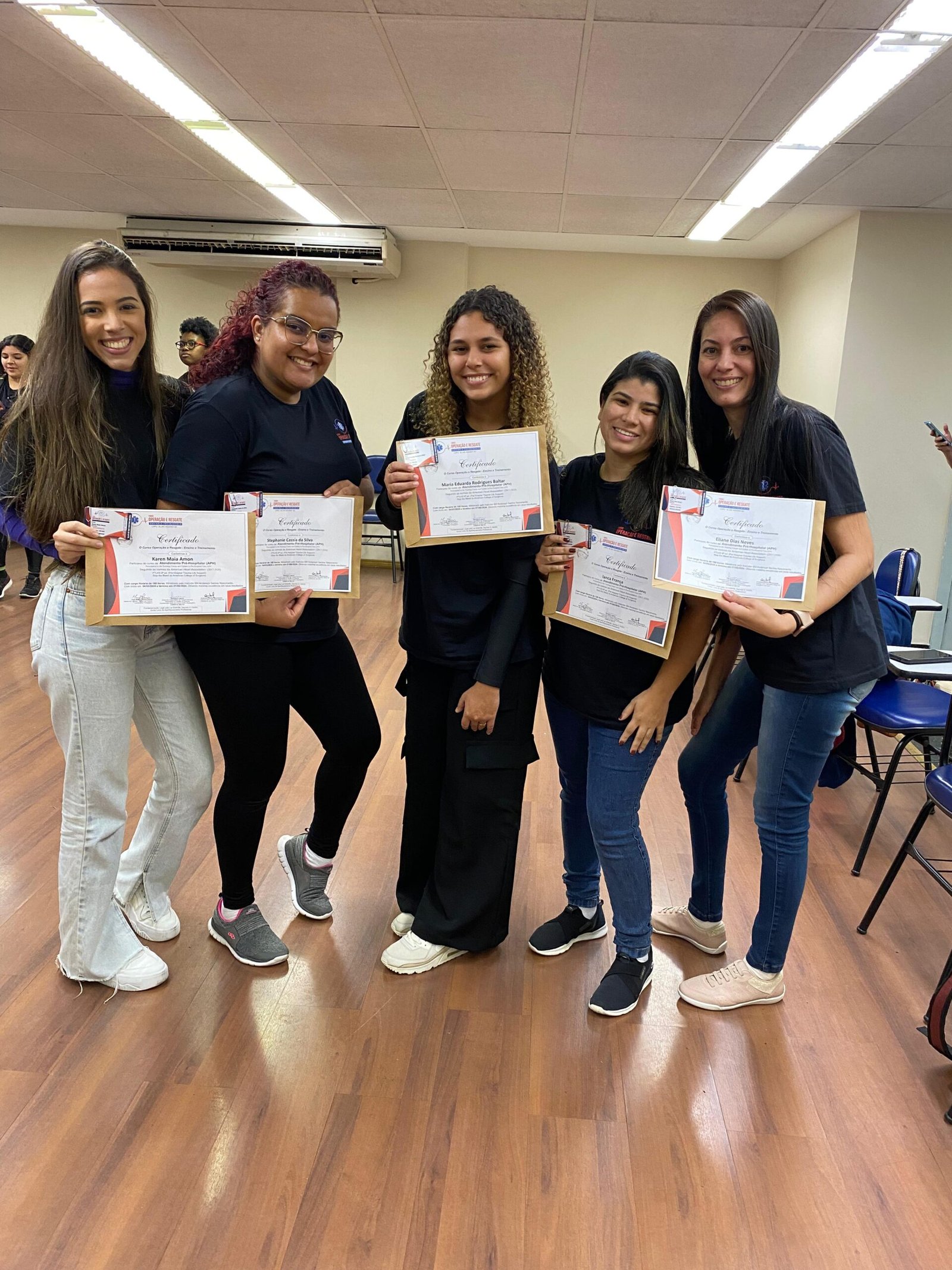 Alunas formadas sorrindo de pé com o certificado do curso